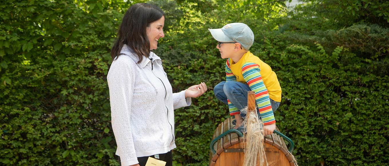 Betreuerin redet mit einem Jungen auf einem Holzpferd